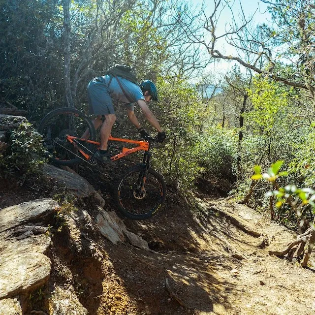 Mountain biker on a full-suspension bike riding down a steep rocky technical section of the Bennett Gap descent in Pisgah National Forest