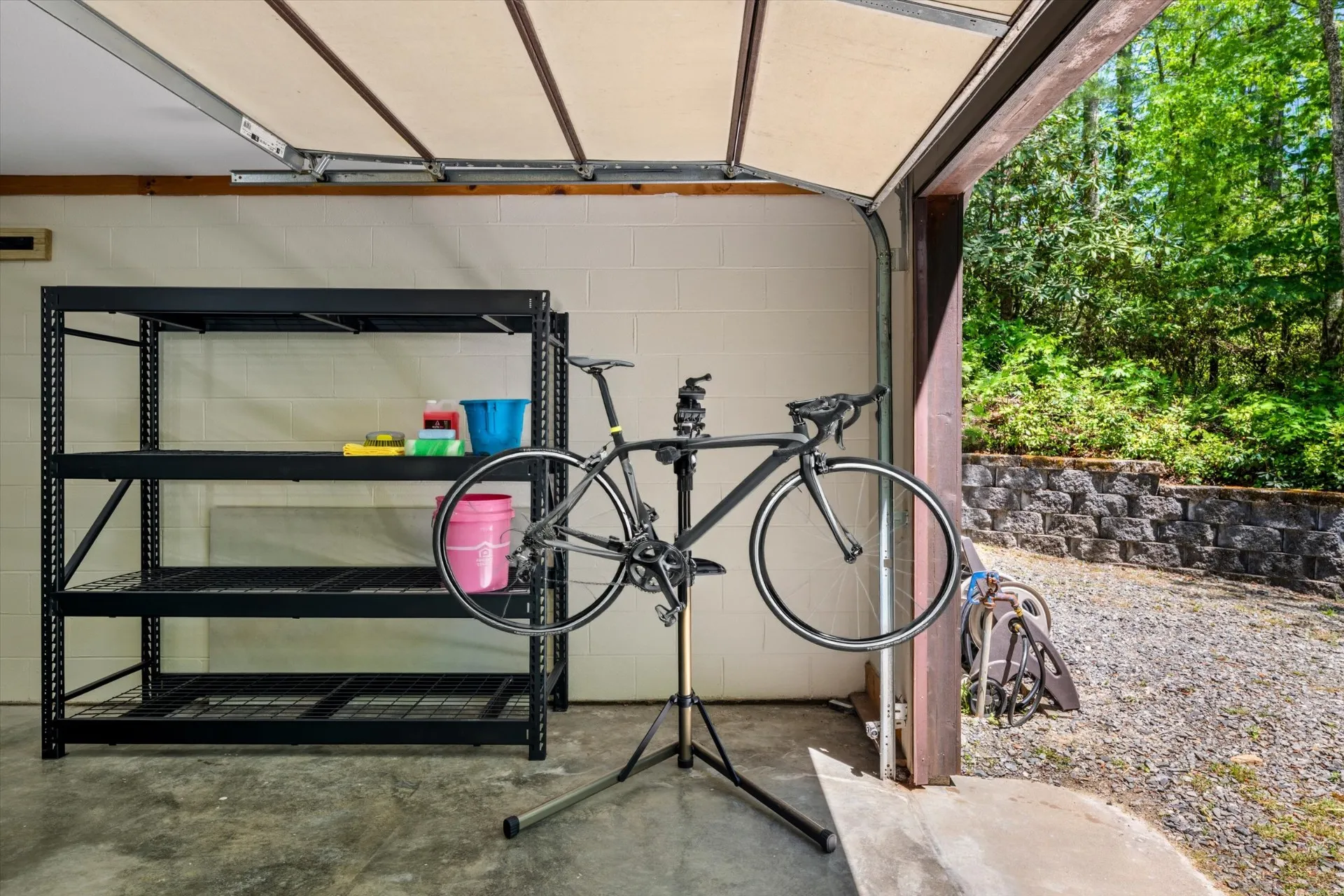 Outdoor bike wash station in the open garage bay with a road bike on a repair stand and wash supplies on a shelf