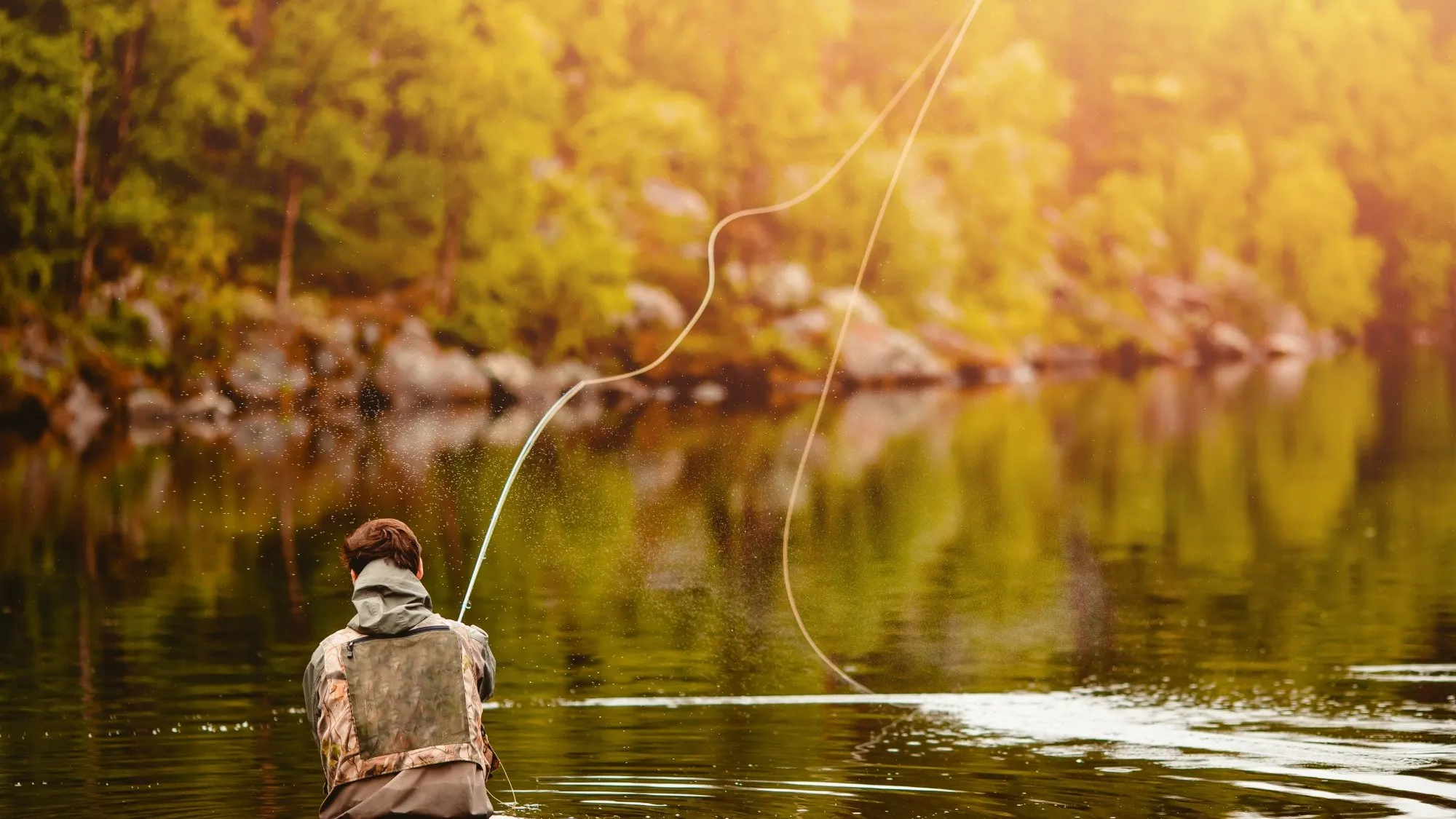 Fly angler in waders casting on a calm pool, the line whipping out across glassy water under golden afternoon light