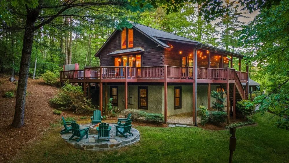 Cabin exterior at twilight with warm porch lights and a stone fire pit ringed by Adirondack chairs