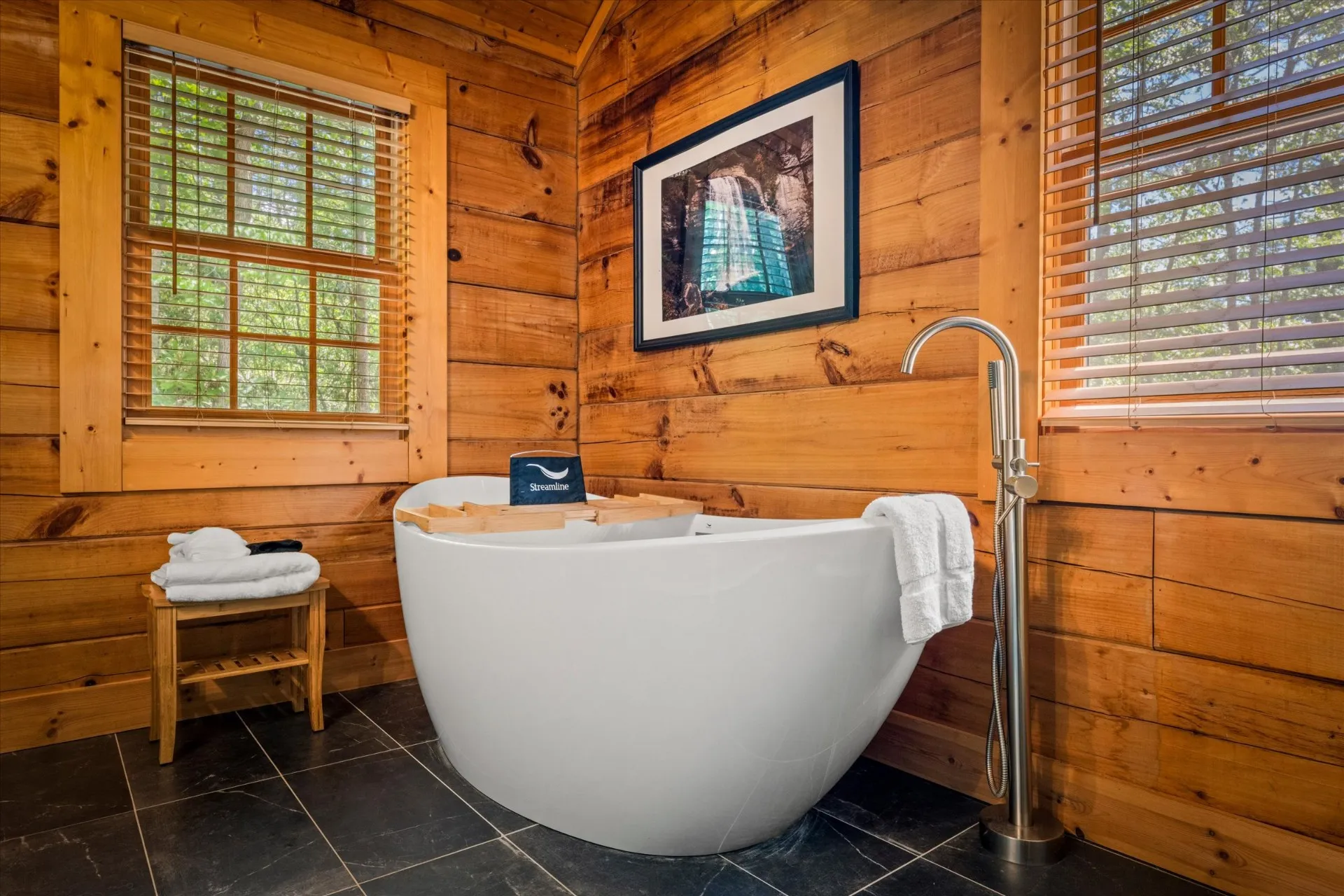 Primary bath with deep freestanding soaking tub, slate tile floor, and forest views through the window
