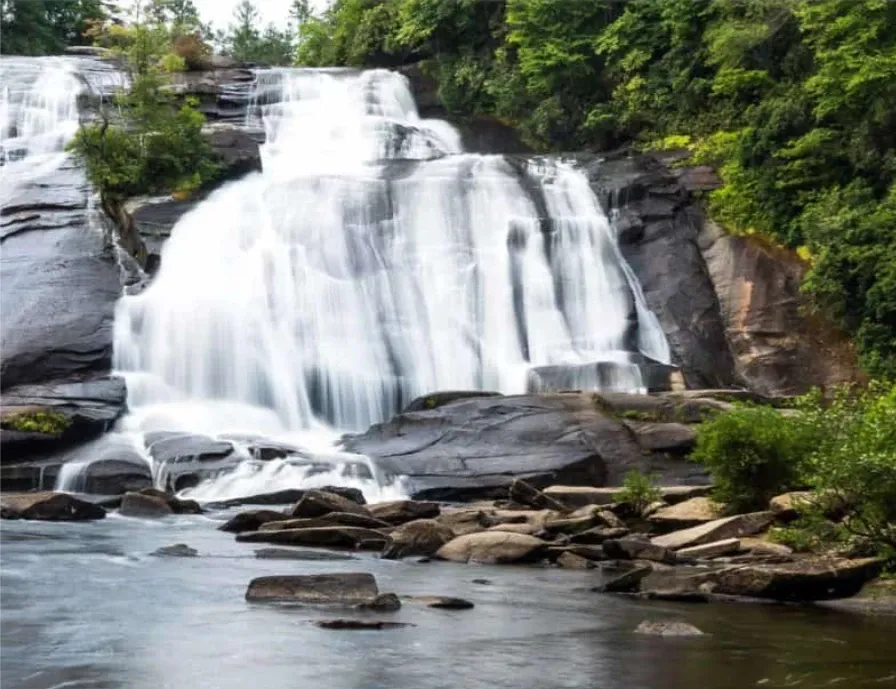 Wide cascade waterfall in DuPont State Forest sliding over a layered granite face into a calm pool below, ringed by rhododendron and forest